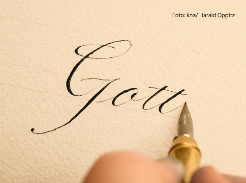 	Eine Person schreibt das Wort Gott mit einer Feder auf weißem Papier.