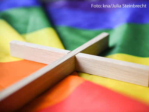 Ein Holzkreuz liegt auf einer Regenbogenfahne. 