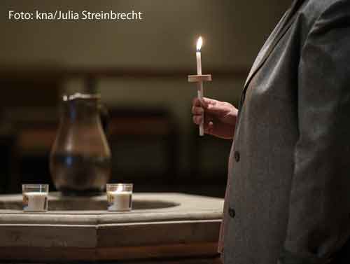 Eine Frau steht einer brennenden Kerze in einer dunklen Kirche. Sie nimmt an einer Osternacht teil.