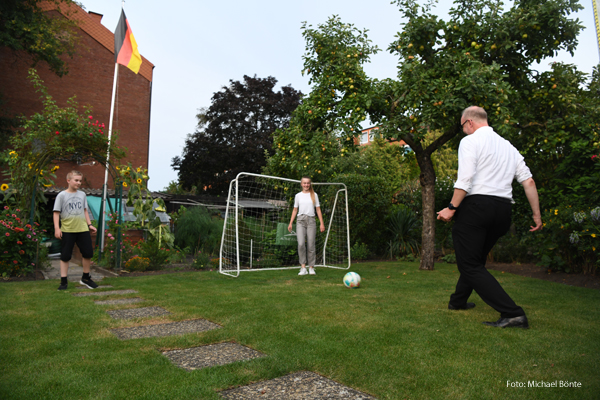 Ein Pfarrer spielt mit Kindern Fußball. 