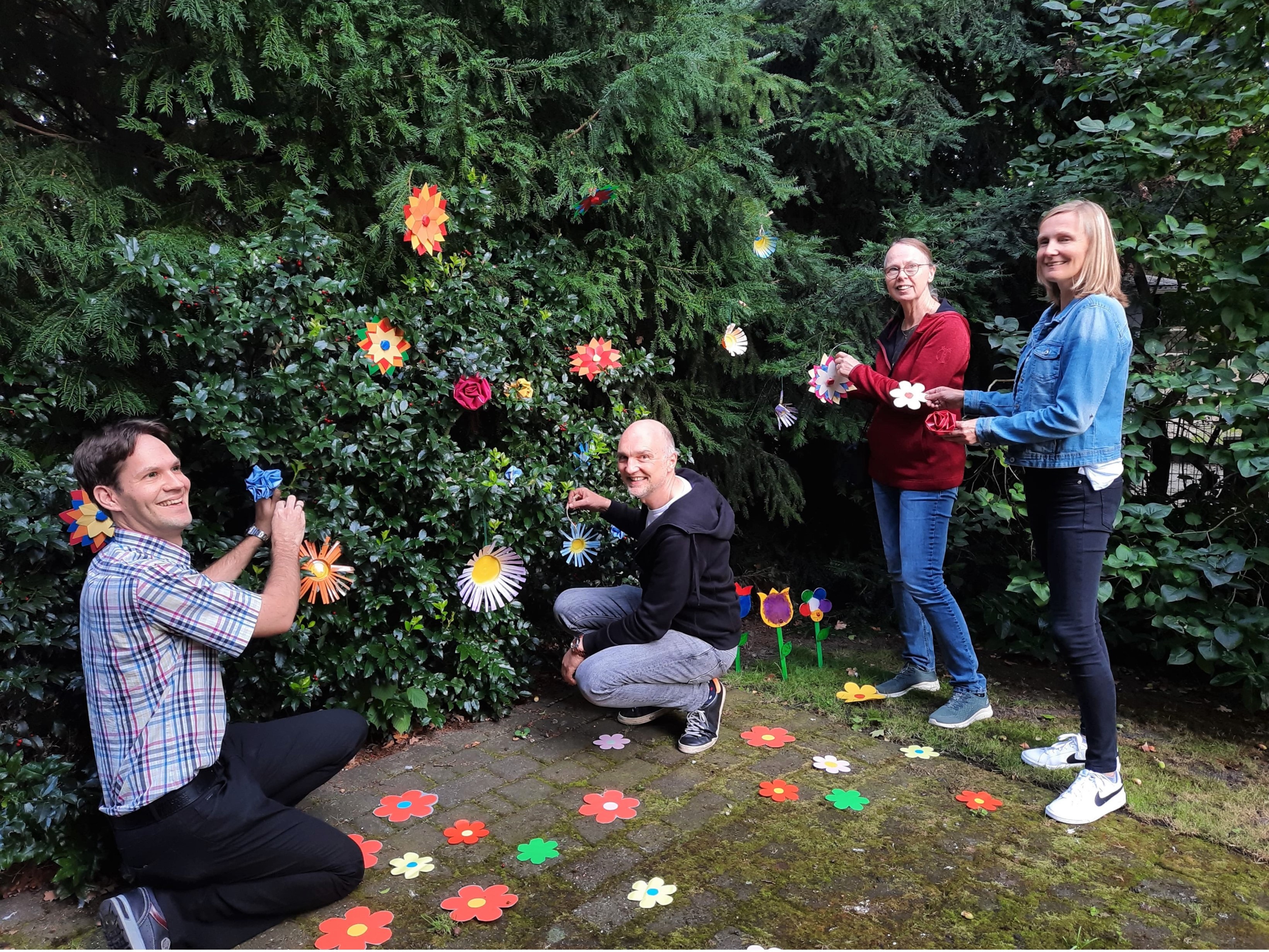 Zwei Männer und zwei Frauen hängen Blumen an eine Hecke,