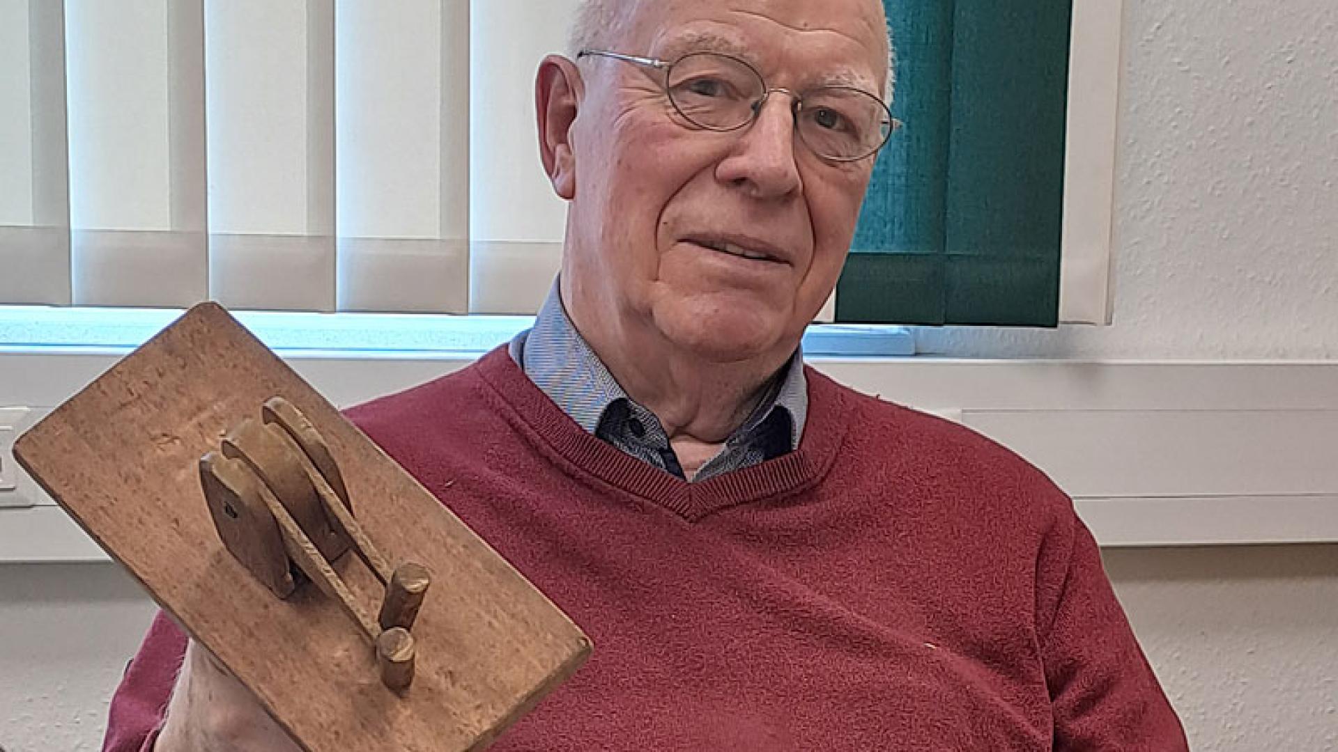 Älterer Mann hält eine hölzerne Kleppe in der Hand