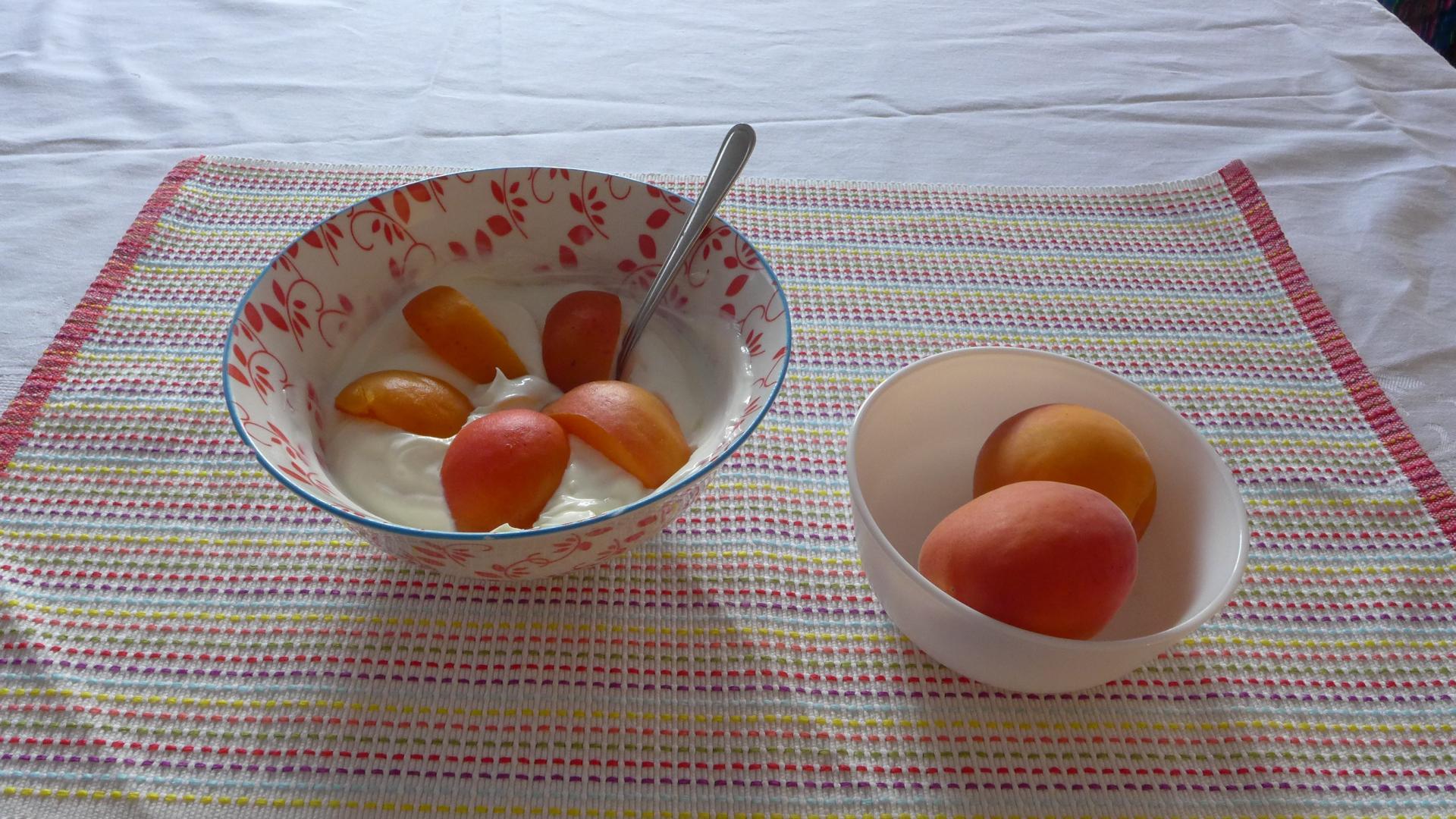 Auf einem Tisch stehen eine Schüssel mit Quark und eine Schüssel mit Aprikosen. 