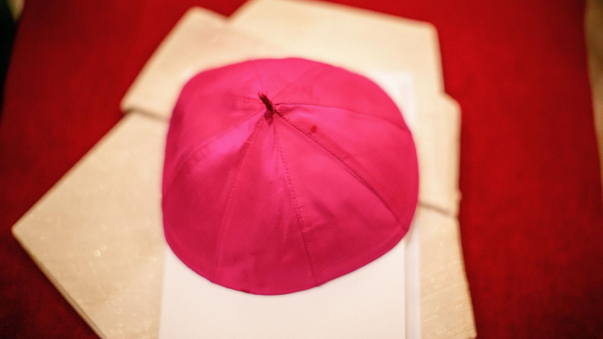 ein violetter Pileolus eines Bischofs liegt auf einer Kirchenbank