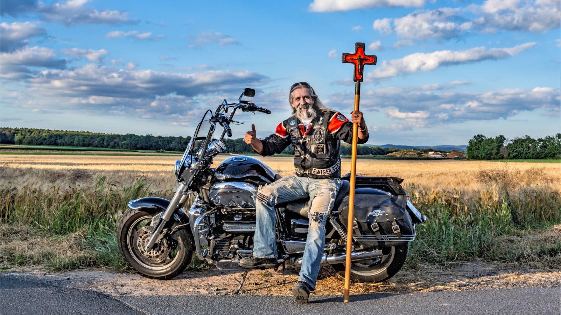 Thomas Draxler von den Jesus-Bikern sitzt auf seinem Motorrad und hält ein Vortragekreuz in der Hand