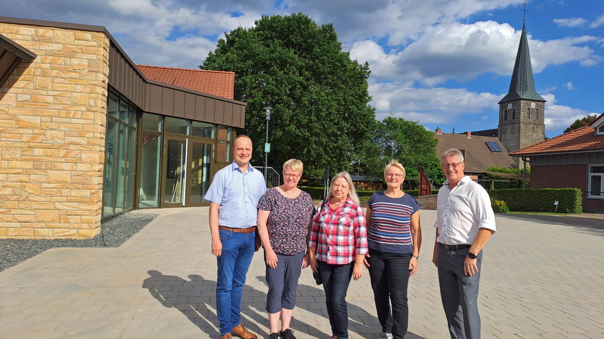 Fünf Menschen stehen auf einem Platz, im Hintergrund ist eine Kirche zu sehen.