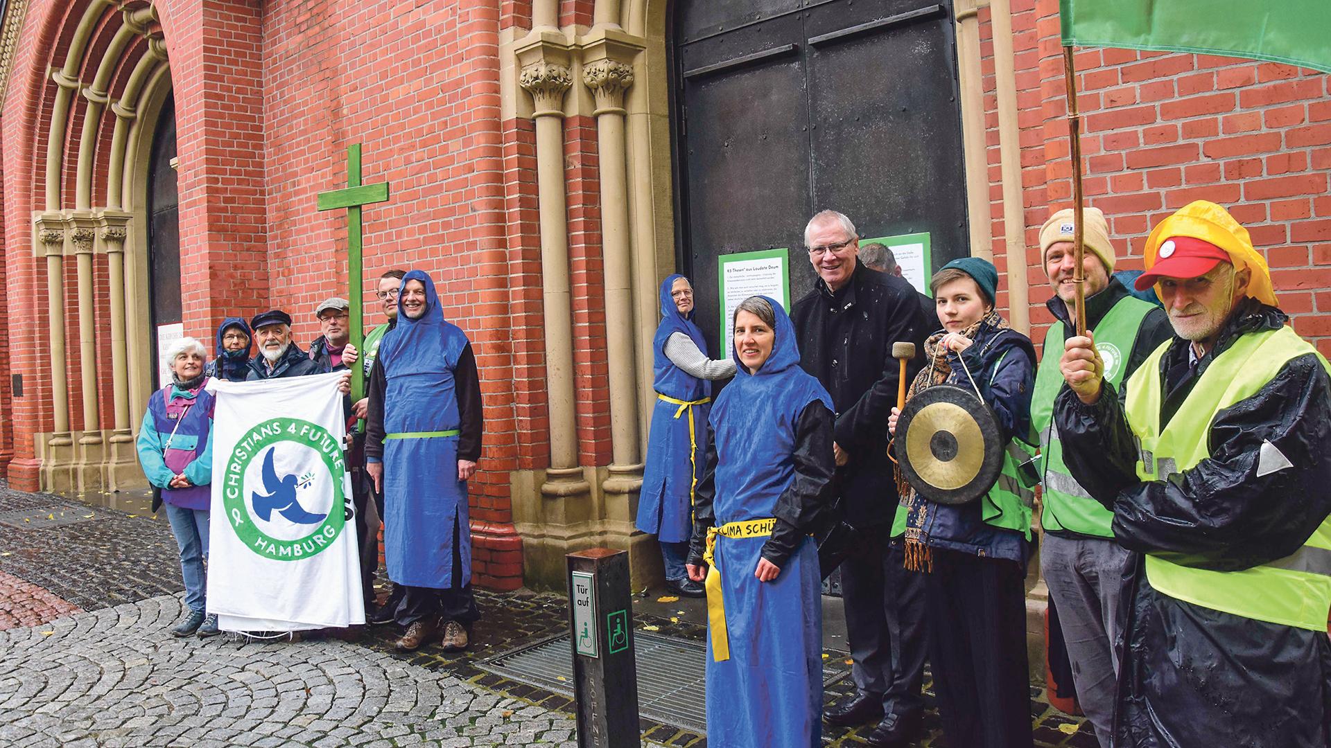 Mit einem Kreuz und Transparenten kamen Erhard Maria Klein und die Christians for Future zum Mariendom. Martina Skatulla schlägt die zweite Thesentafel an. Dompropst Berthold Bonekamp hat gegen diese Protestaktion nichts einzuwenden.