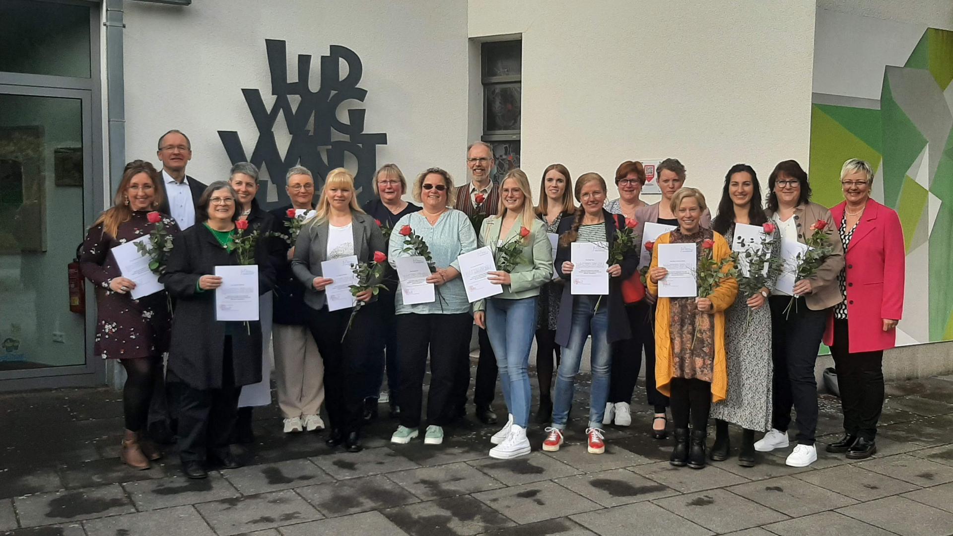 Eine Gruppe von Menschen steht vor einem Haus, viele von ihnen halten einen Zettel in die Kamera