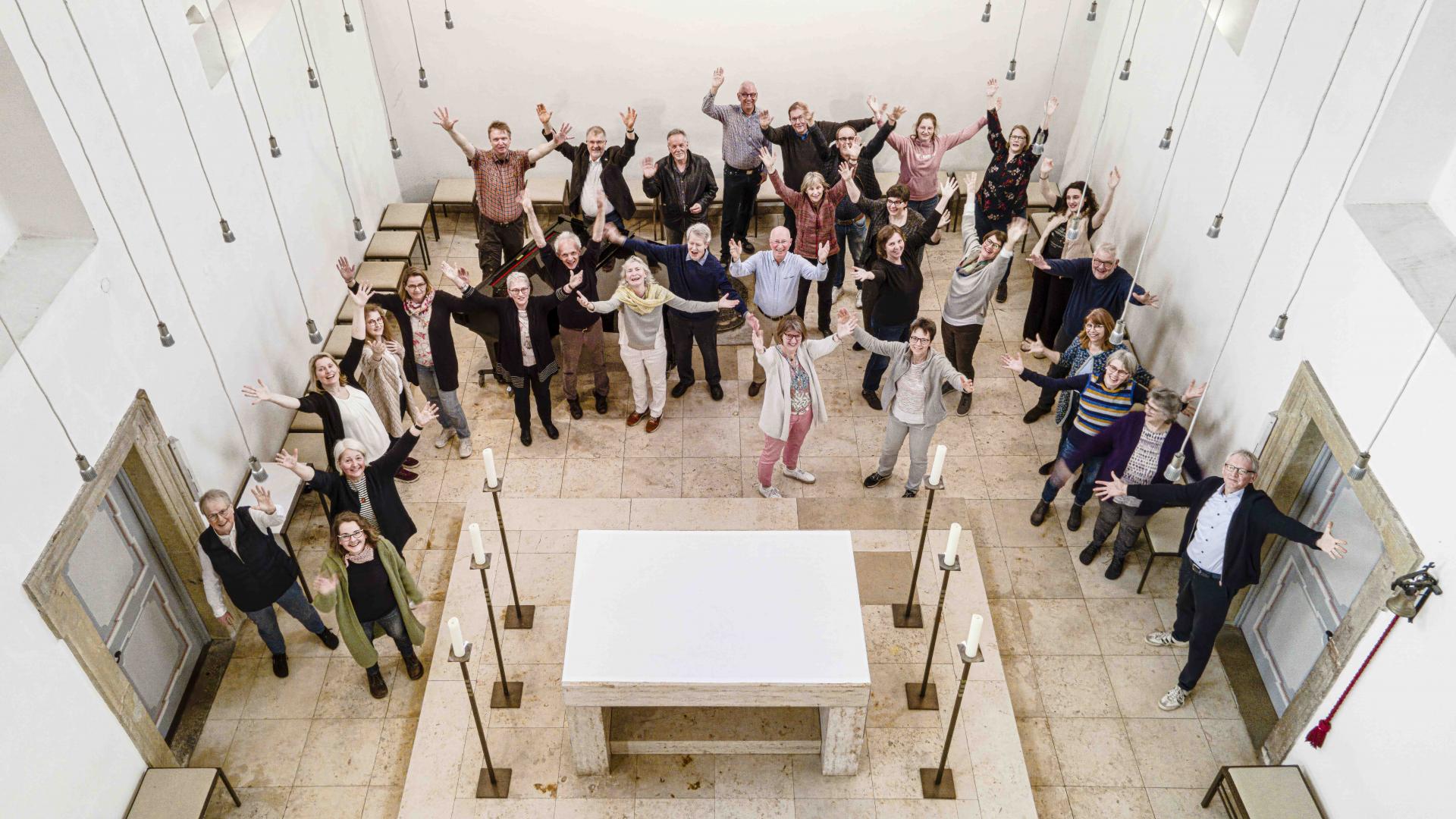 Eine Gruppe von Menschen steht im Altarraum einer Kirche und hebt die Hände