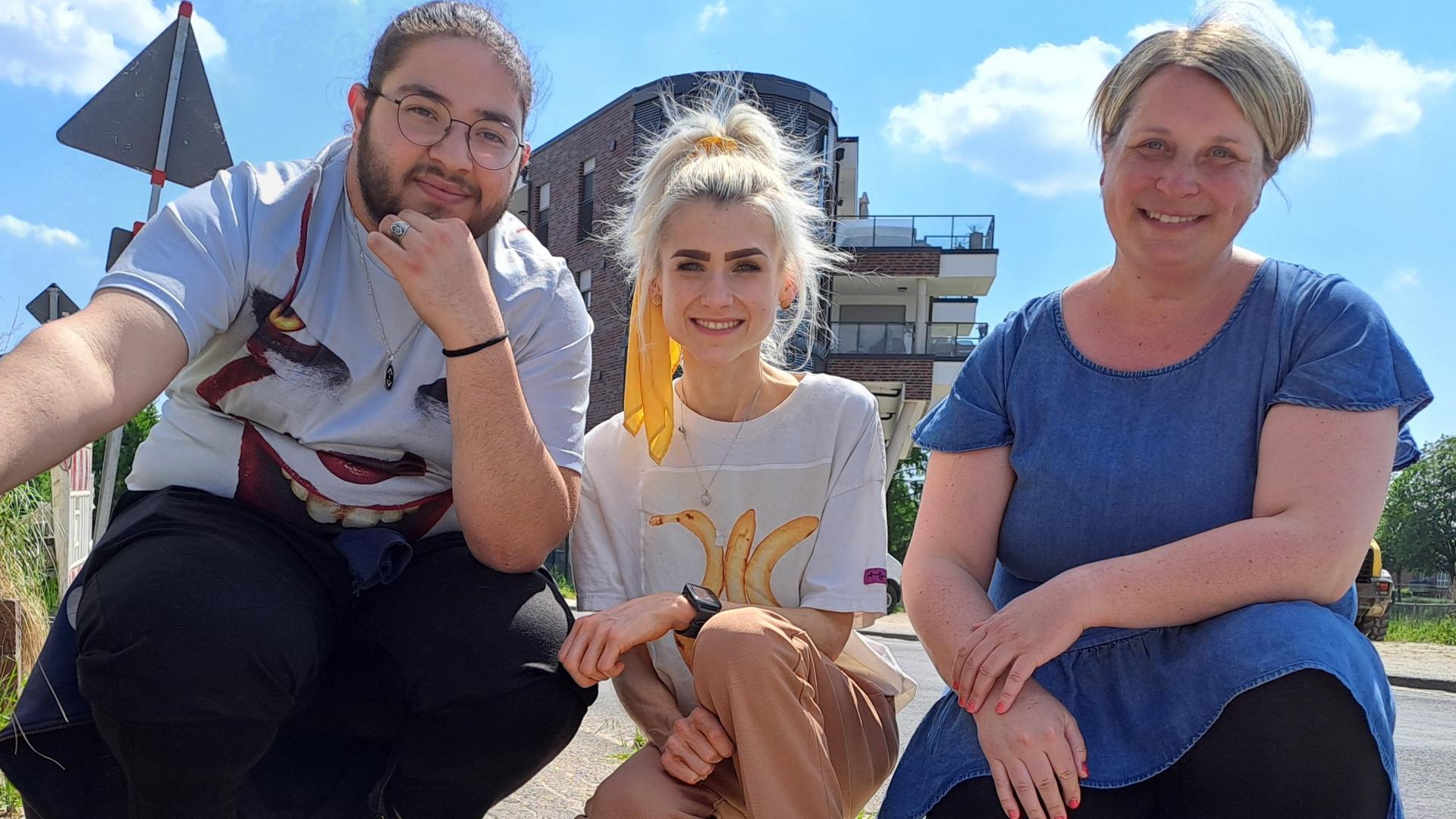 drei Menschen hocken auf einem Bürgersteig